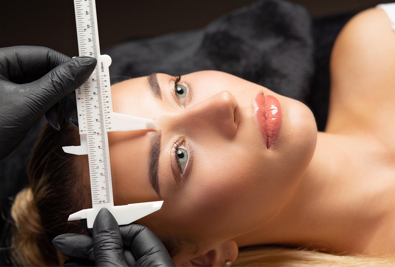Brow artist in black gloves measuring a client's eyebrows with a brow ruler before shaping